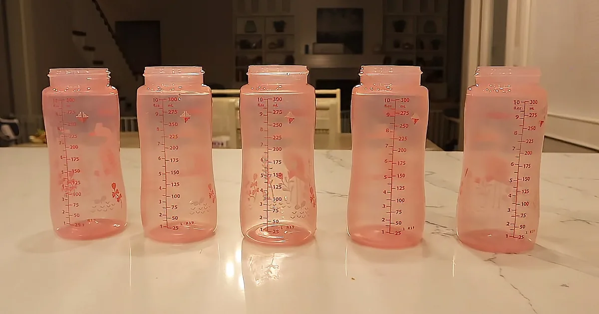 Five pink baby bottles with measurement markings on a white countertop.