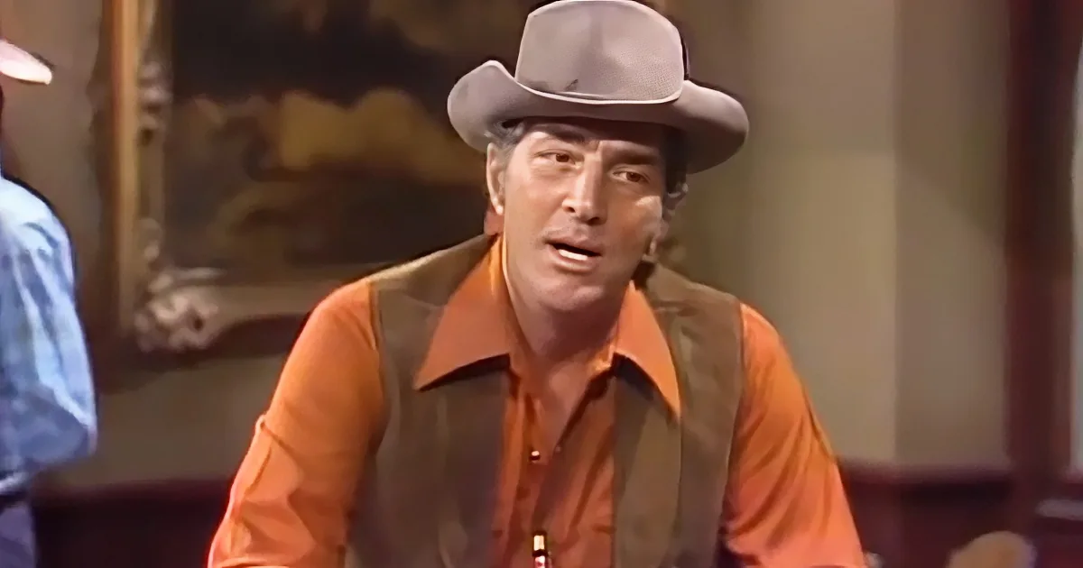 A man in a cowboy hat and orange shirt is speaking, with another person partially visible on the left.