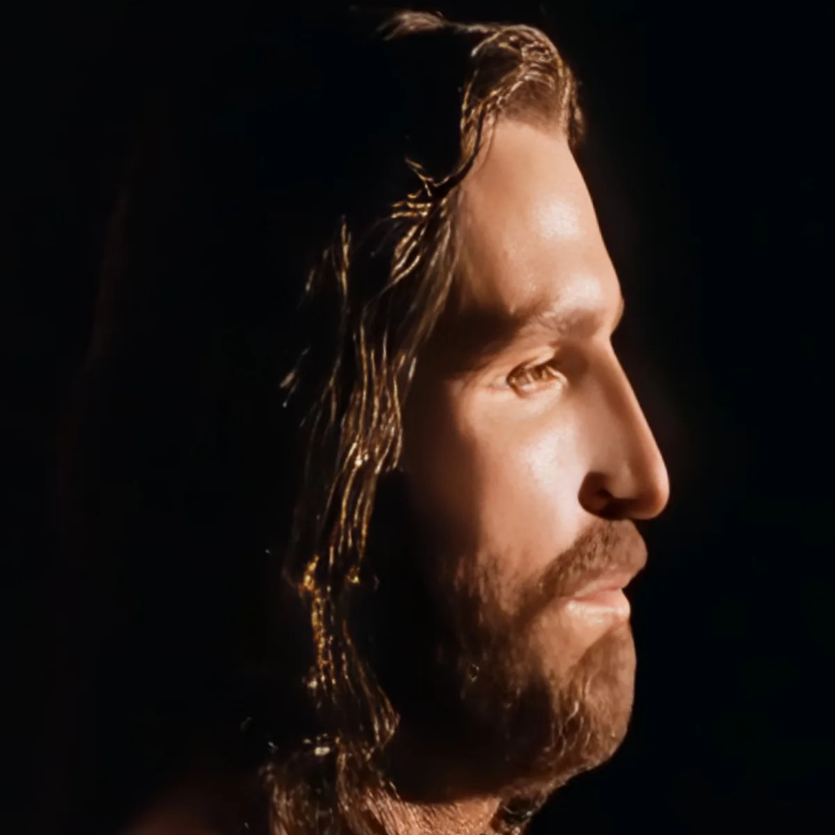 A man with long hair and a beard, gazing upward in a dimly lit setting.
