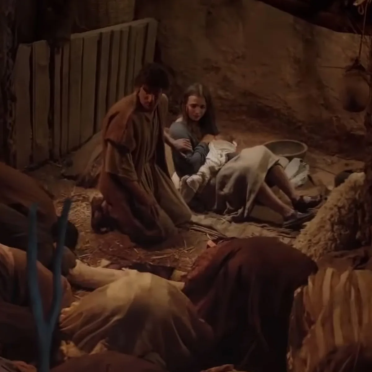 Mary holds baby Jesus as Joseph kneels beside them in a rustic stable setting.