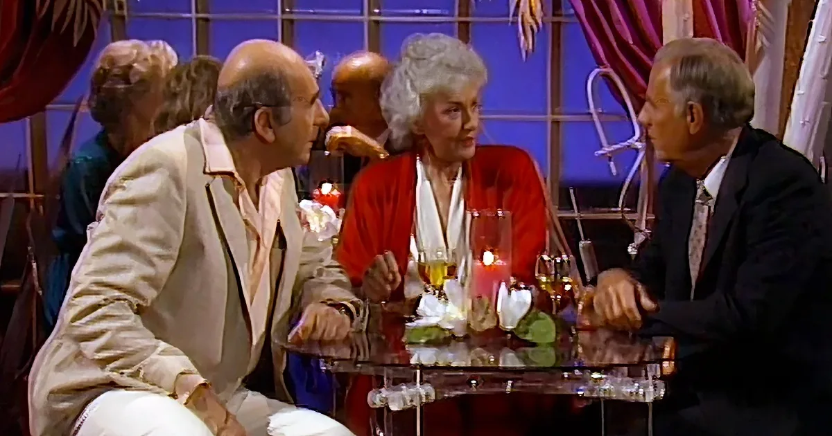 Three older adults are seated at a table with drinks and candles, engaged in conversation.