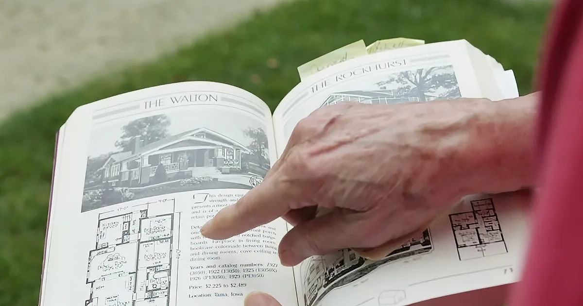 An elderly person points at a house design in a catalog.
