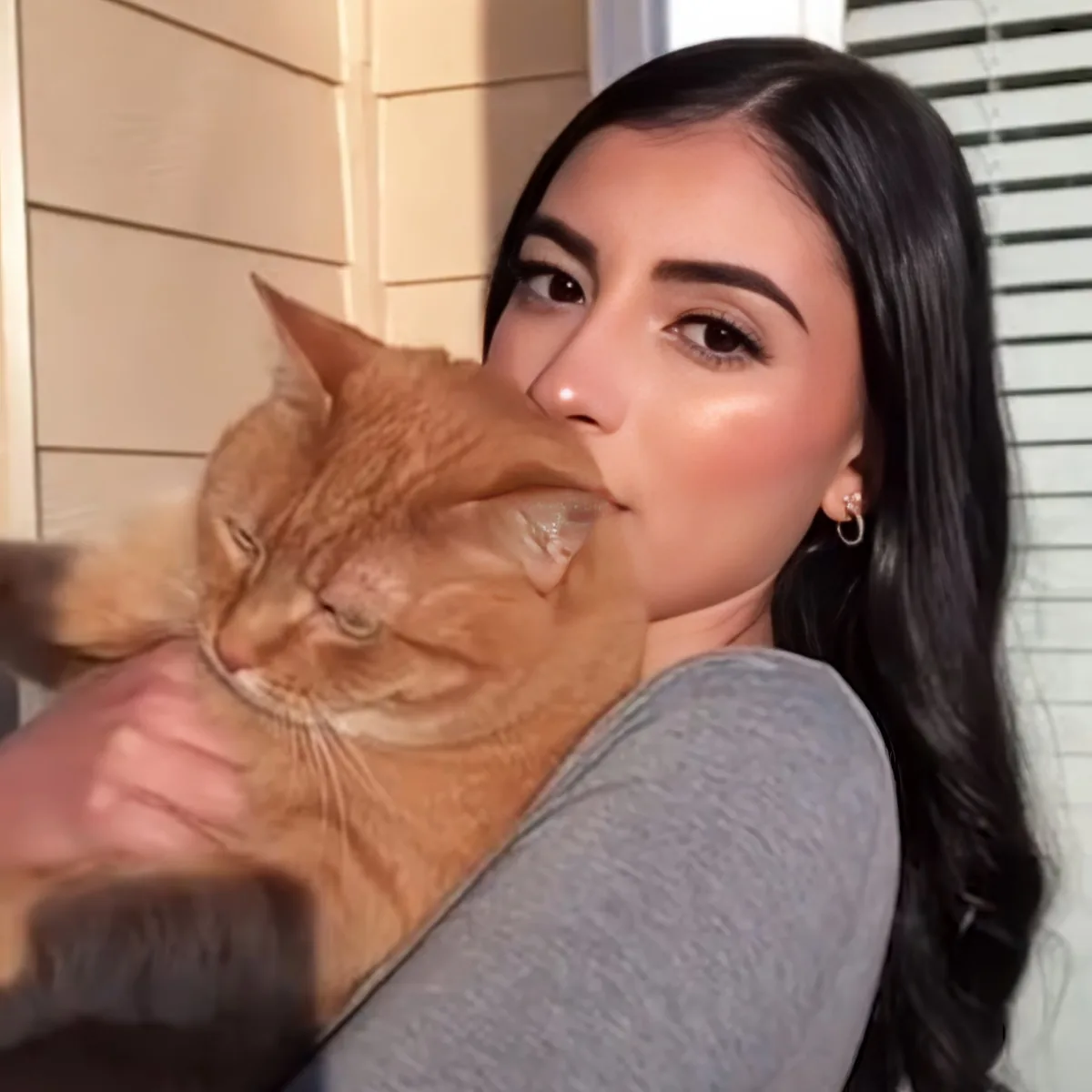 A woman holds a large orange cat close to her face, both appearing relaxed.