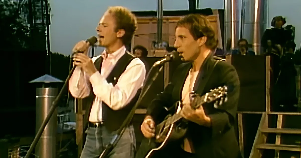 Two men perform on stage, one singing into a microphone, the other playing guitar.