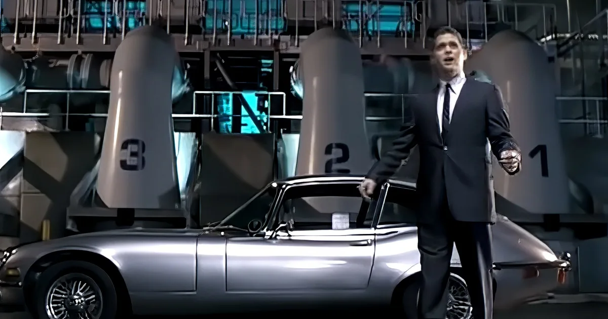 A man in a suit stands beside a silver car, with large countdown clocks in the background.