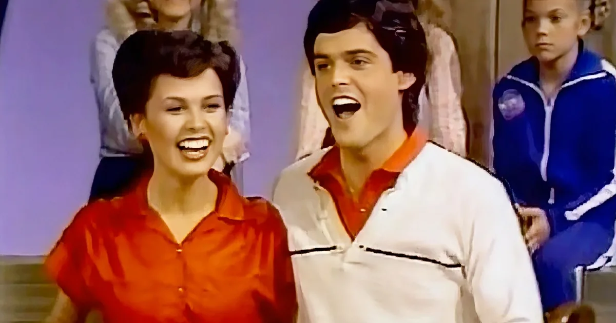 A man and woman in vibrant outfits are smiling and laughing together, with a child in the background.