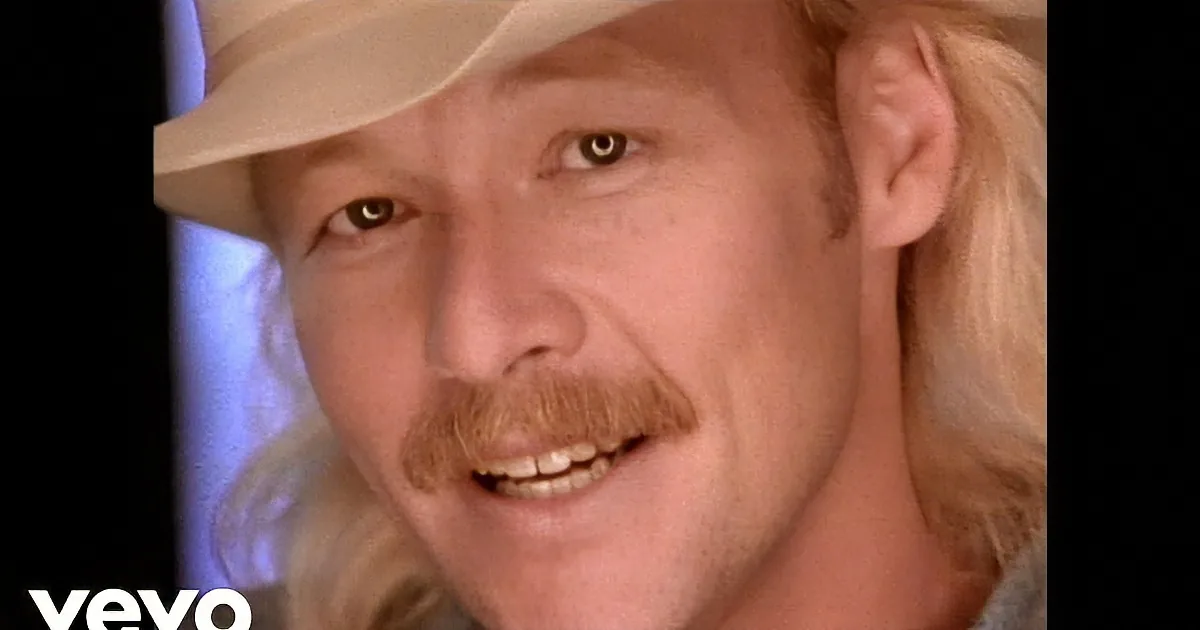 A smiling man with long blonde hair, wearing a cowboy hat and a patterned shirt, is the main subject.