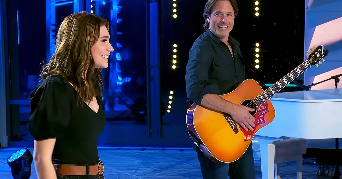 A woman smiles at a man holding an acoustic guitar on a stage with blue lighting.