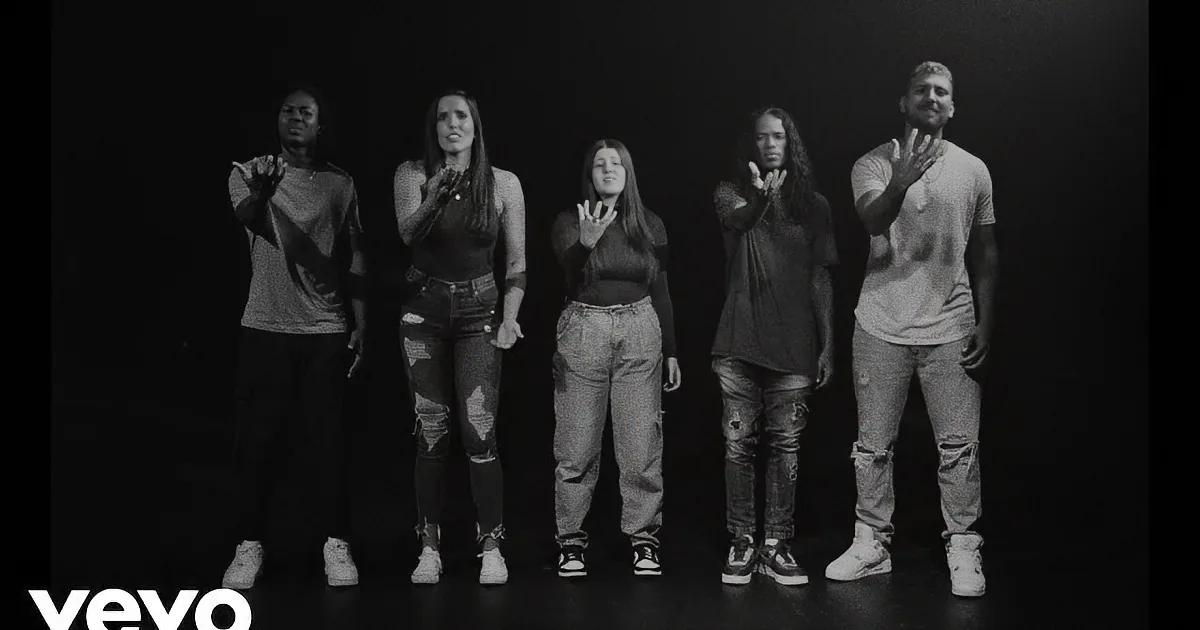 Five individuals in casual attire stand in a row, hands raised, against a dark background.