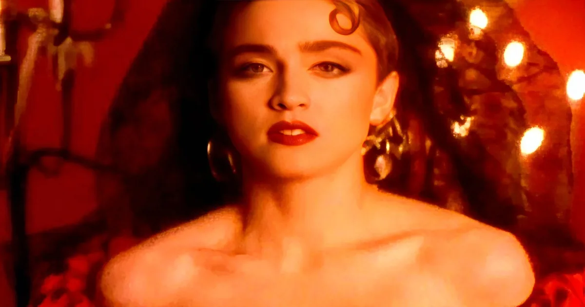 A woman with red lipstick and large earrings stands in a dimly lit, red-hued environment.