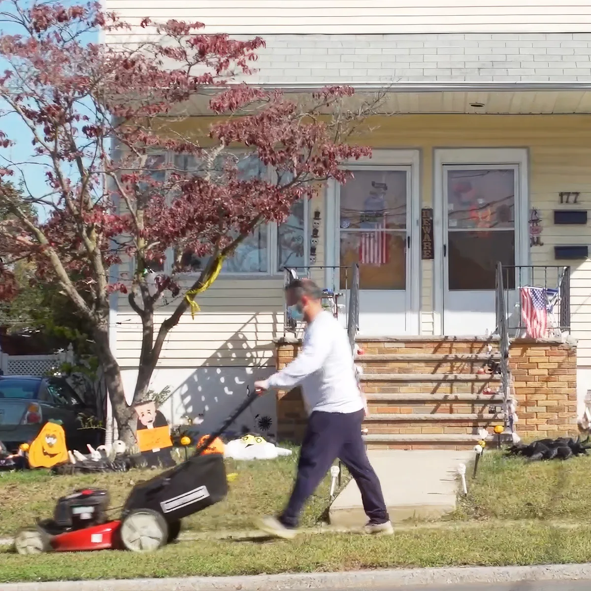 A man mows the lawn in front of a house decorated with Halloween and patriotic themes.