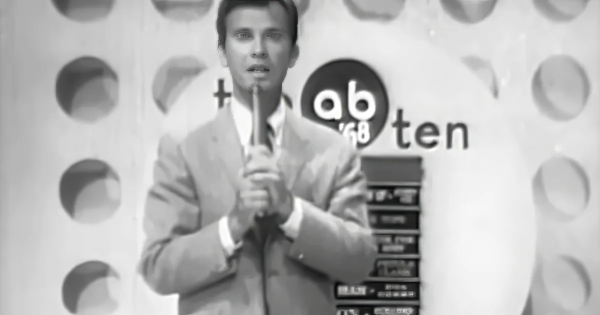 A man in a suit holds a microphone, standing in front of a backdrop with "ab 68 ten" and circular patterns.