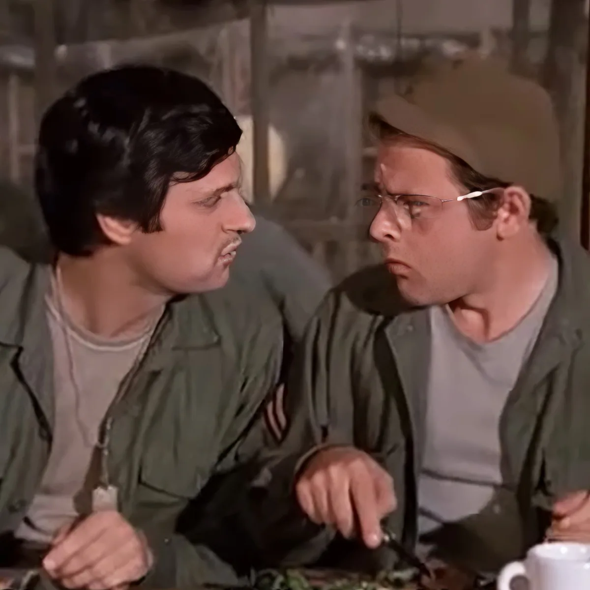 Two men in military uniforms are engaged in a conversation, one pointing while the other listens intently.