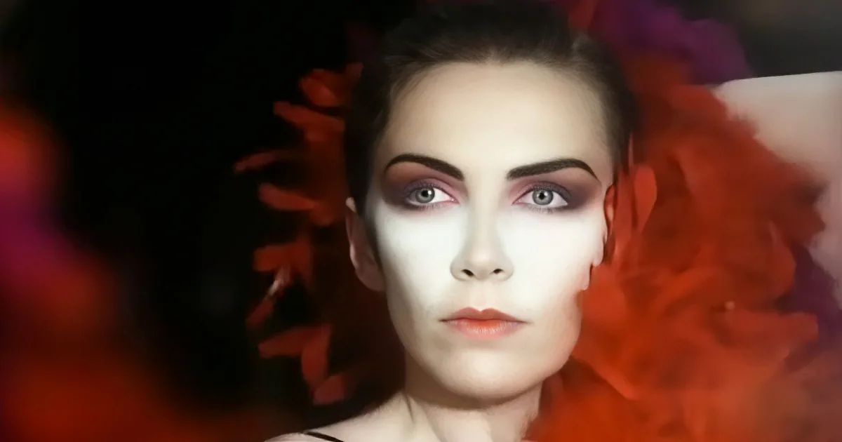 A person with white face paint and red feathers in their hair.