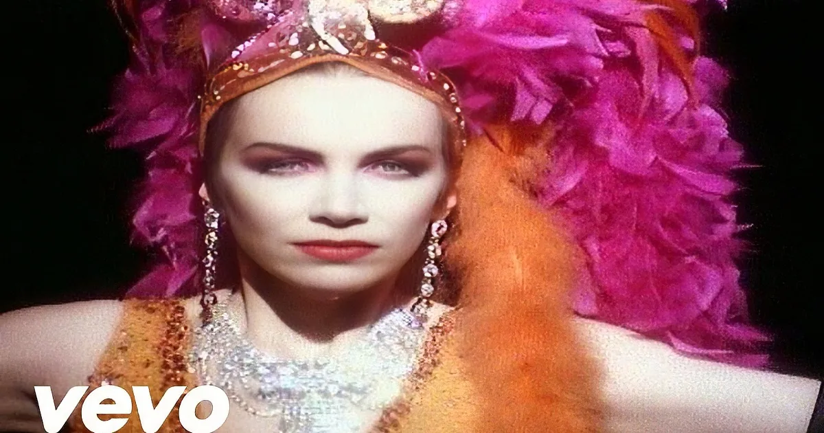 A woman in a glamorous outfit with a crown, feathers, and dramatic makeup.