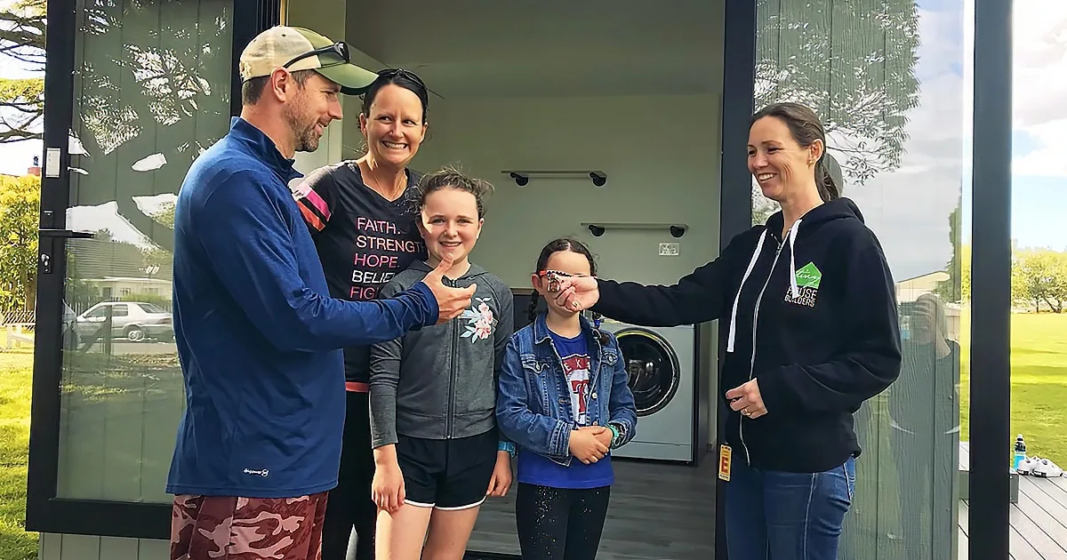 A family of five stands together in front of a modern home, smiling and interacting warmly.