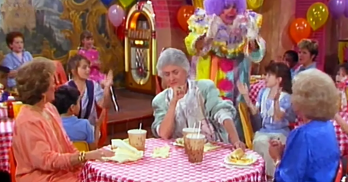 A woman sits at a table with a red-and-white checkered tablecloth, surrounded by children and balloons, appearing to be...