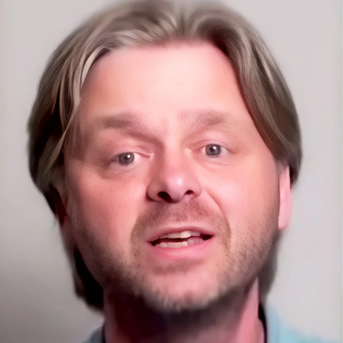 A man with long, light brown hair and a light beard is speaking.