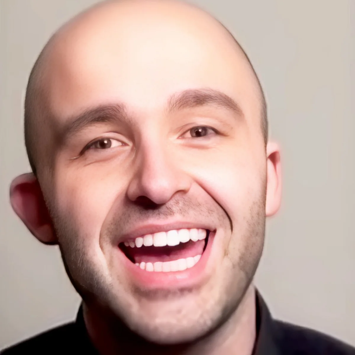 A smiling man with a bald head and a black shirt against a plain background.