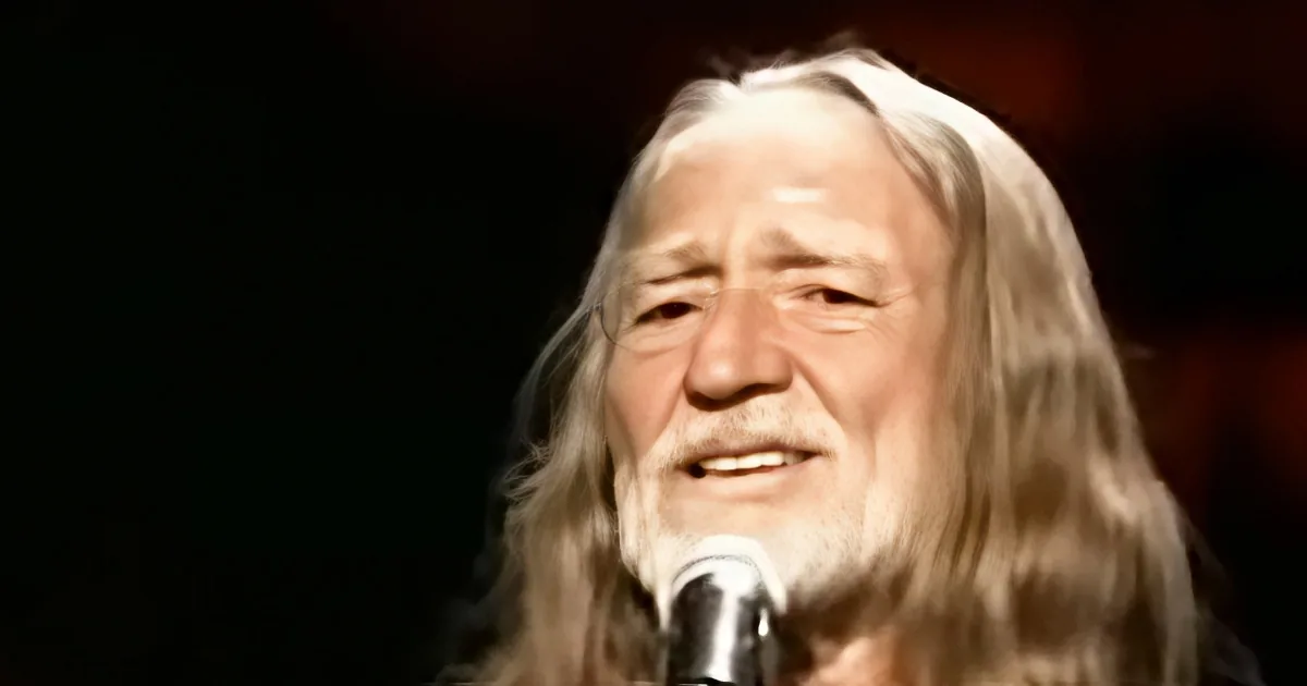A person with long, light-colored hair and a beard is singing into a microphone.