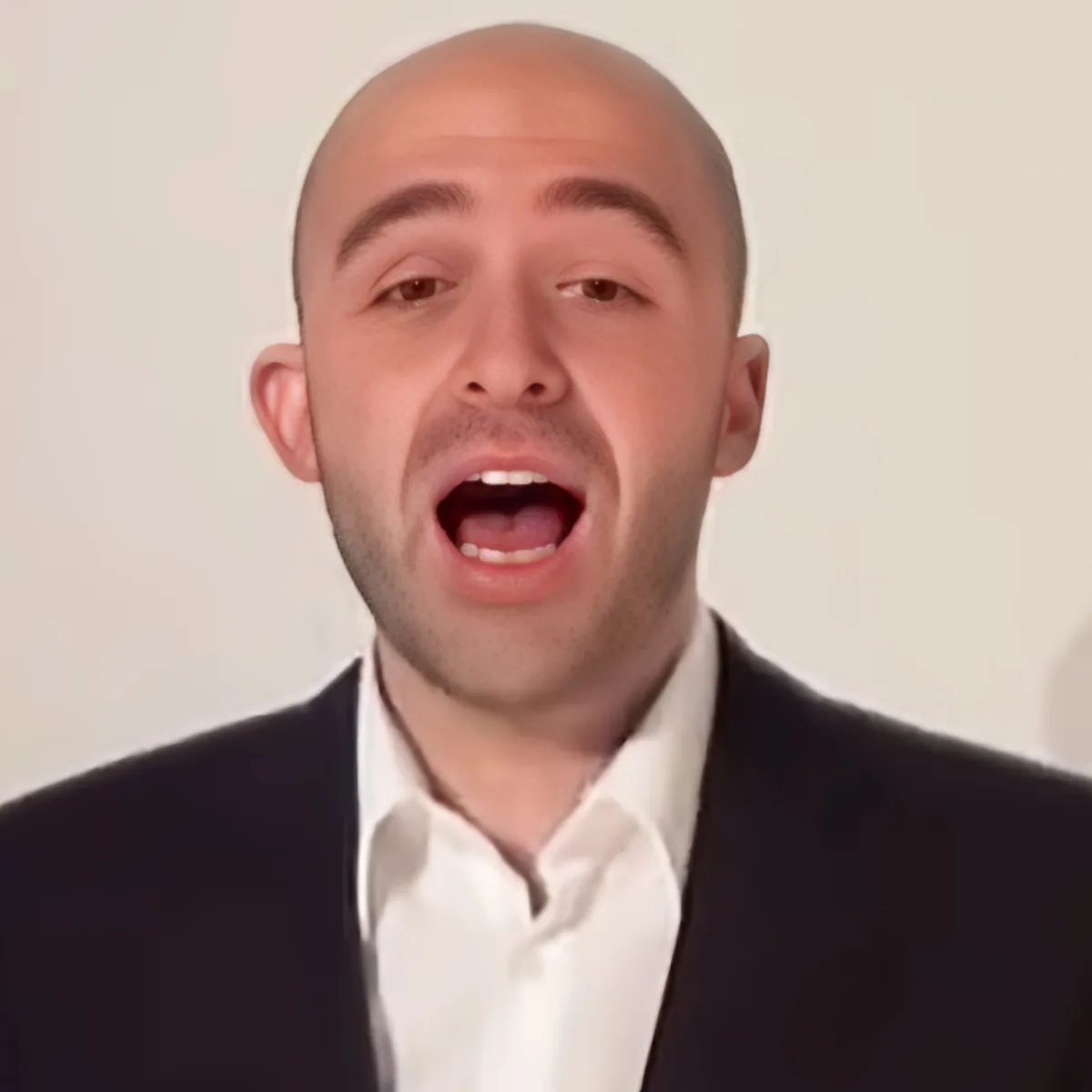 A man in a suit and white shirt is making a loud, open-mouthed expression.