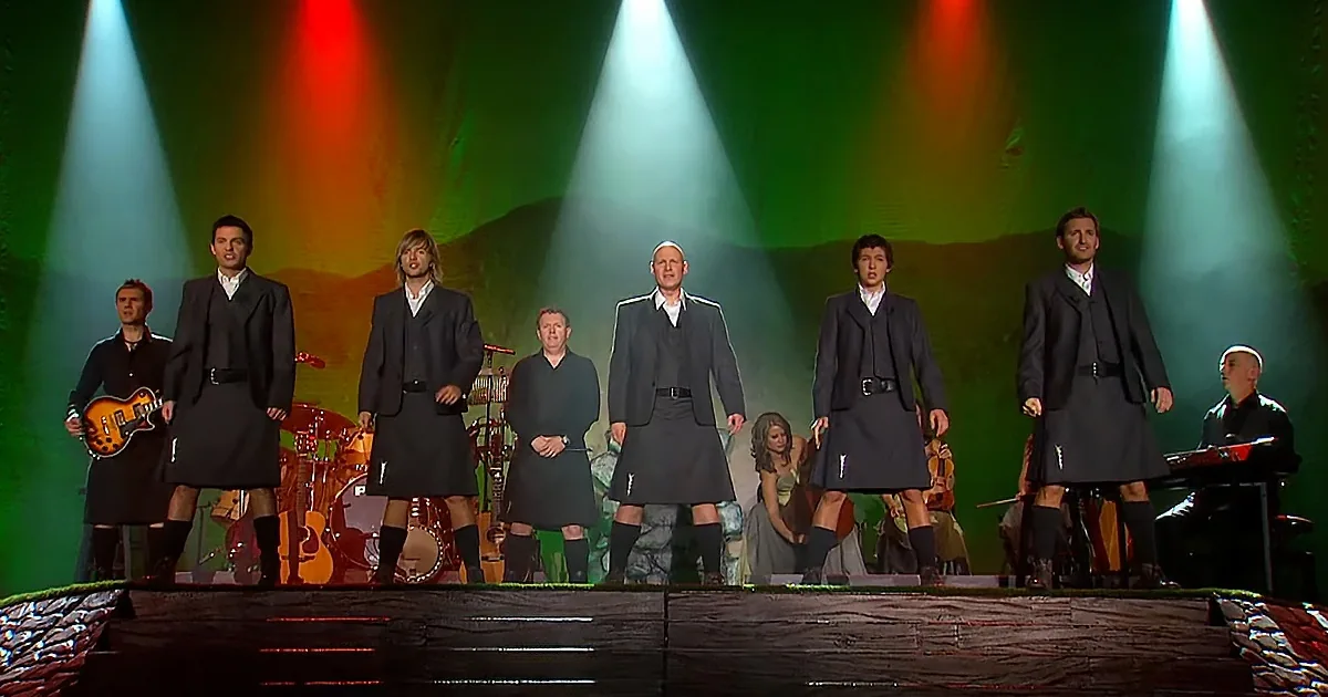 A group of men in kilts performs on stage under colorful spotlights.