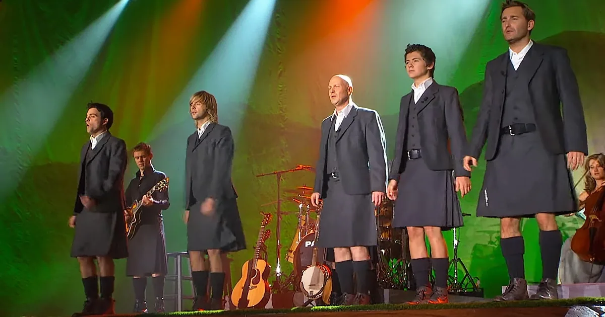 A group of men in kilts and suits perform on stage with musical instruments.