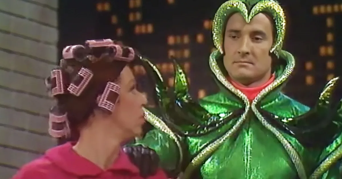 A person in a green sequined costume with a crown stands beside another person with curlers in their hair.