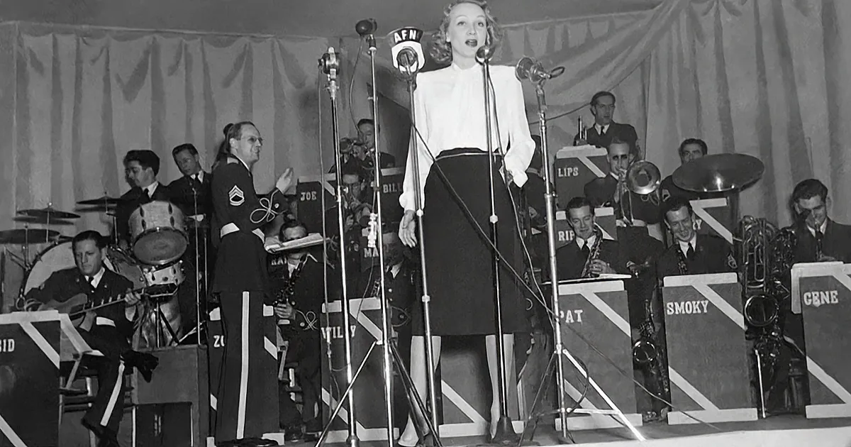 A woman sings on stage with a band, surrounded by microphones and musical instruments.