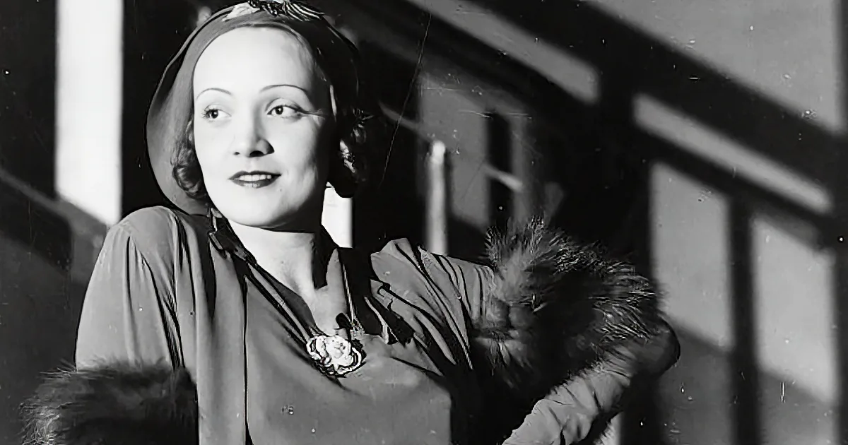 A woman in a vintage outfit with fur details and a floral necklace, smiling.