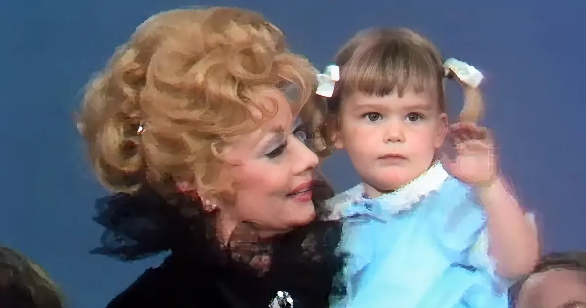 An older woman with voluminous blonde hair holds a young child in a blue dress with pigtails.