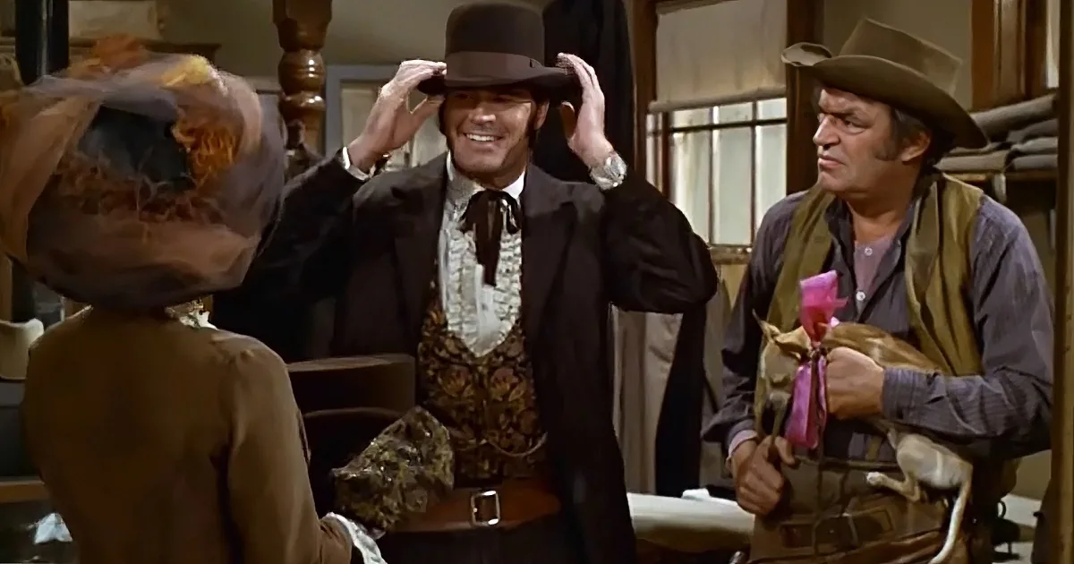 A man in a cowboy hat and vest adjusts his hat while another man in a cowboy hat and vest looks on.