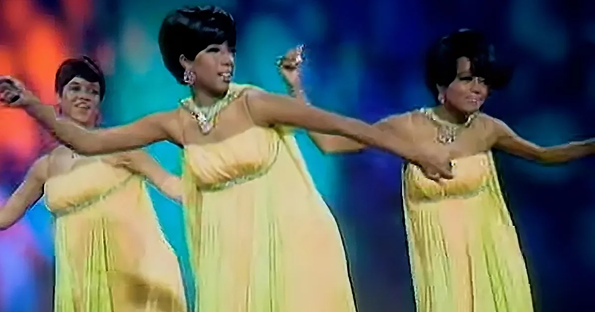 Three women in yellow dresses perform a synchronized dance with vibrant stage lighting.