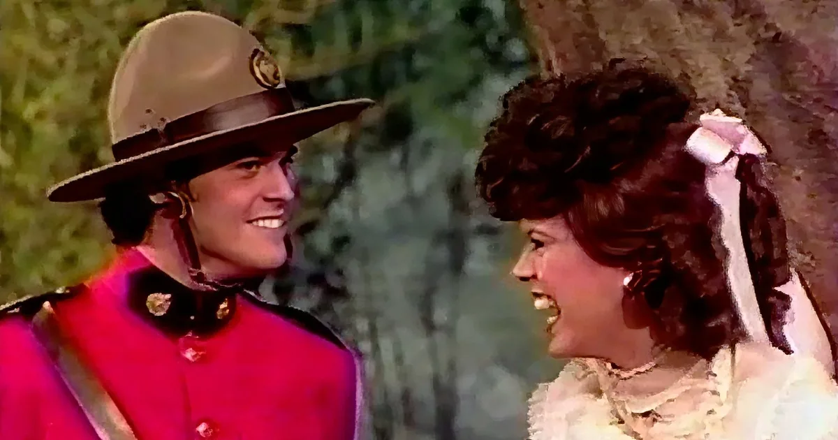 A man in a red uniform and hat smiles at a woman in a white dress with a bow, both appearing happy.