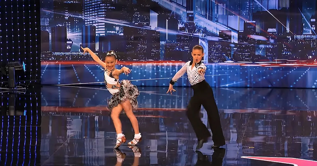 Two young dancers in a cityscape setting, one in a white and black outfit, the other in black pants and a white shirt...