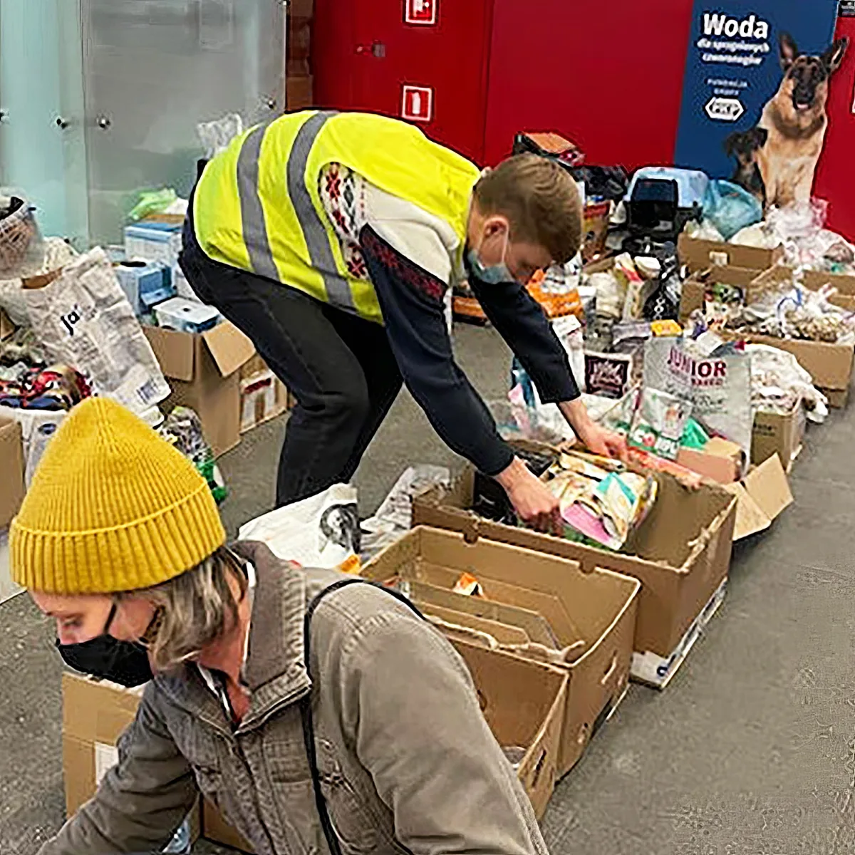 A man in a yellow vest sorts through boxes of donated items in a warehouse.
