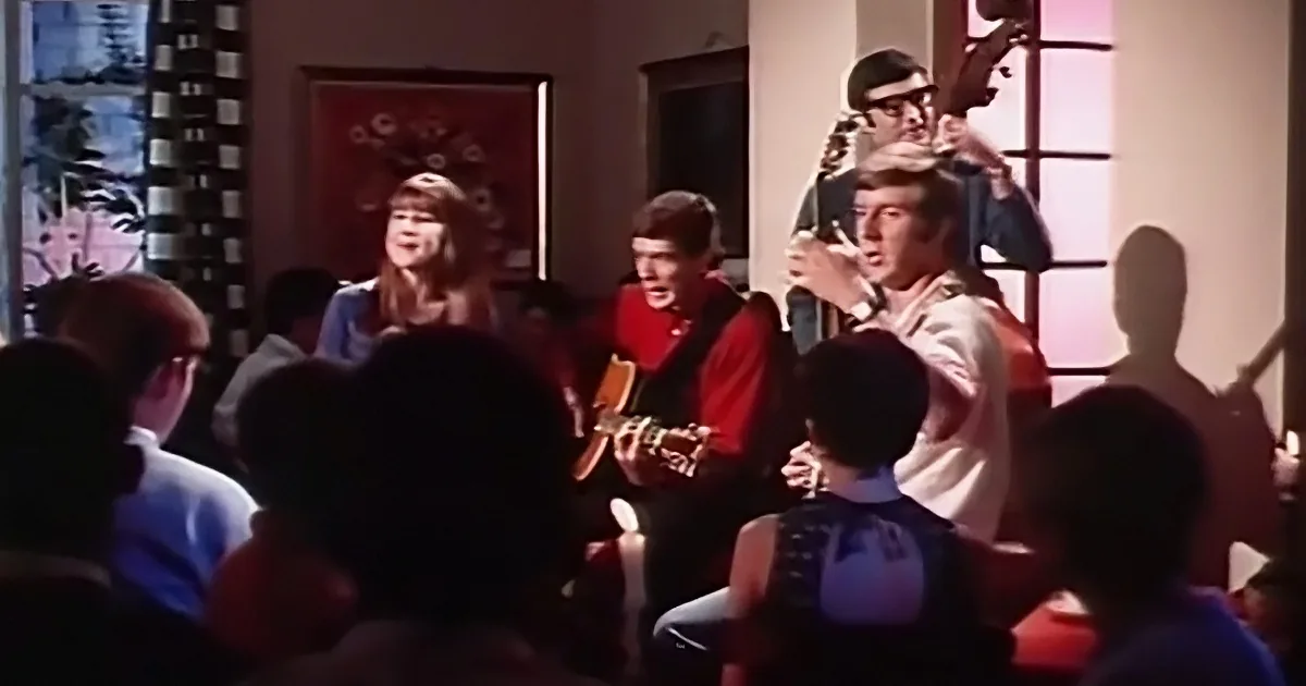 A band performs on stage with a guitarist, drummer, and singer, surrounded by an audience.
