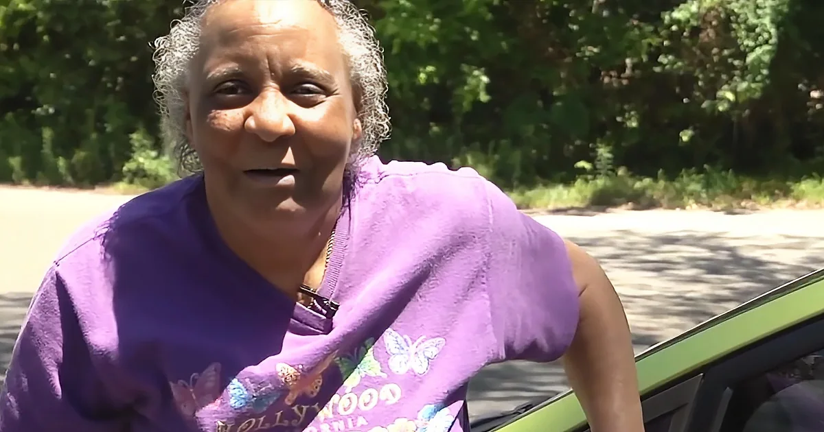 A woman in a purple "Hollywood" shirt stands outdoors, with trees and sunlight in the background.