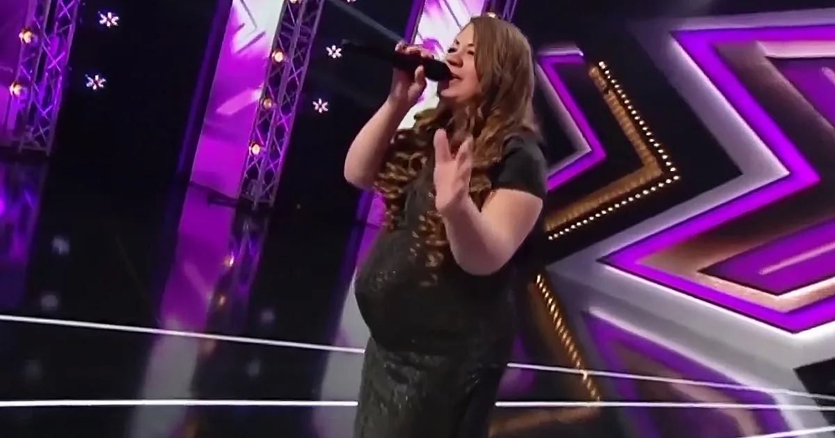 A woman in a black dress sings into a microphone on a stage with purple and white lights.