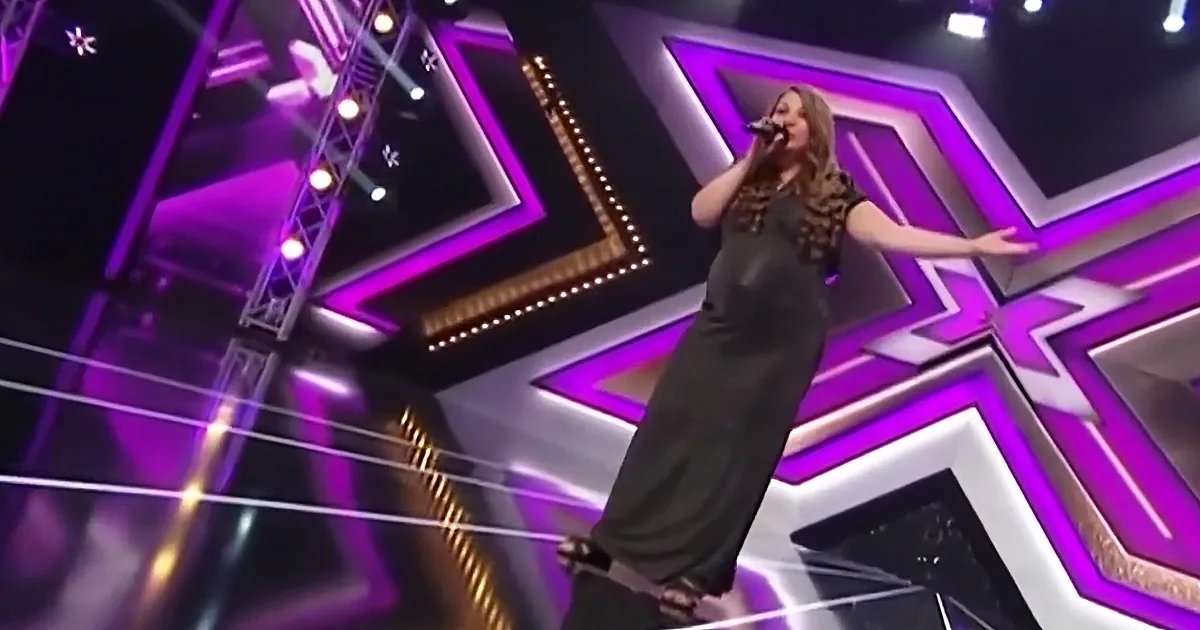 A woman in a black dress sings on a stage with purple and white geometric patterns.