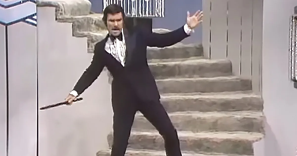 A man in a black suit and white shirt holds a knife, striking a dramatic pose on stone steps.