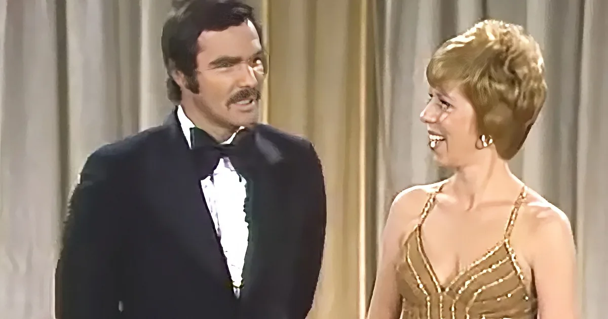 A man in a tuxedo and a woman in a gold dress are smiling and looking at each other.
