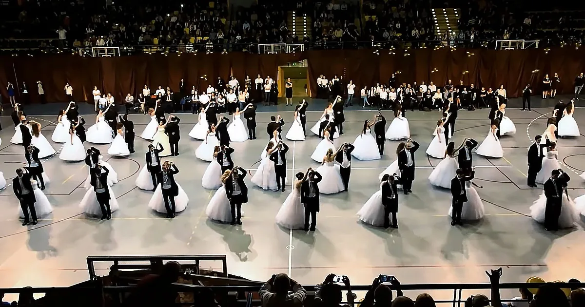 A grand ballroom scene with couples in formal attire, women in white dresses, and men in tuxedos, performing a...