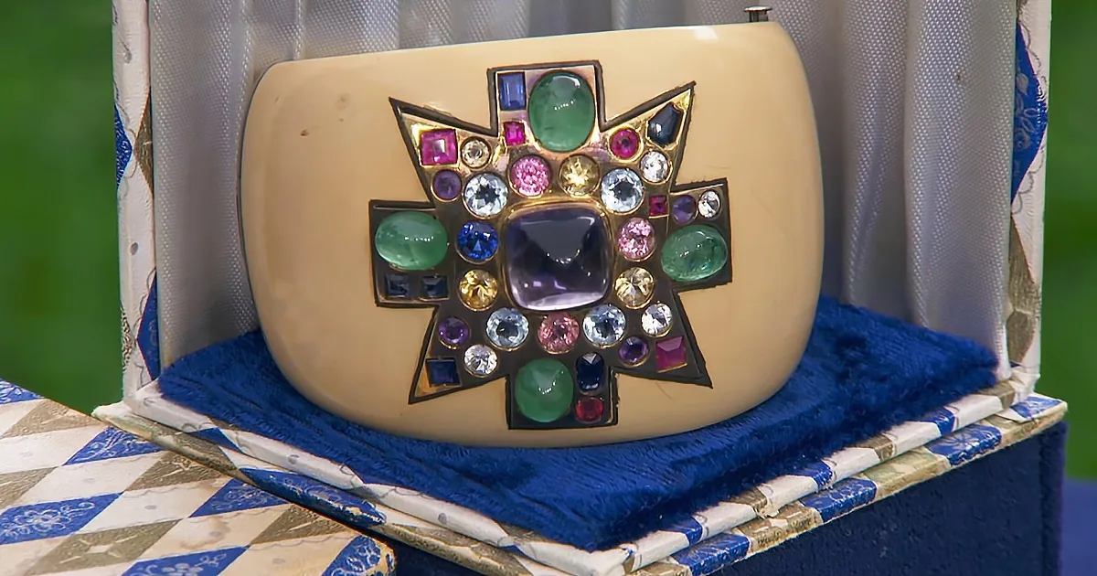 A cream-colored clutch adorned with colorful gemstones is displayed on a blue and white patterned surface.