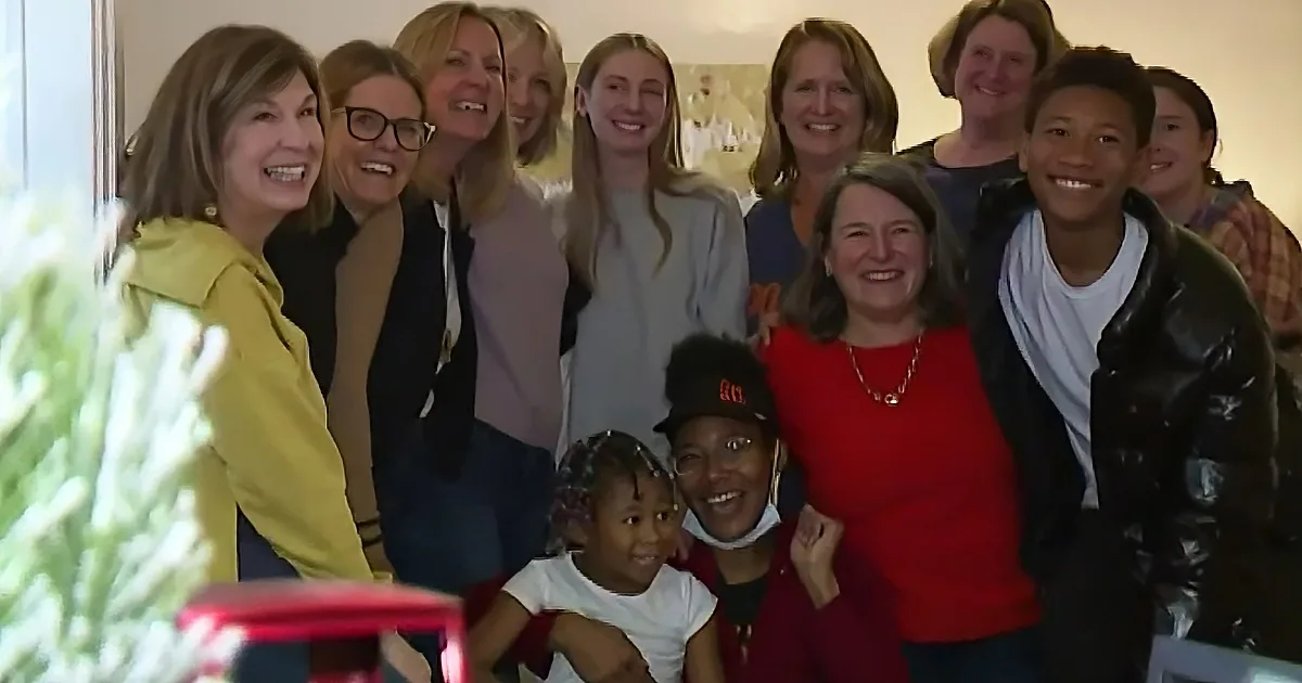 A group of smiling people, including children and adults, gather for a festive photo near a Christmas tree.