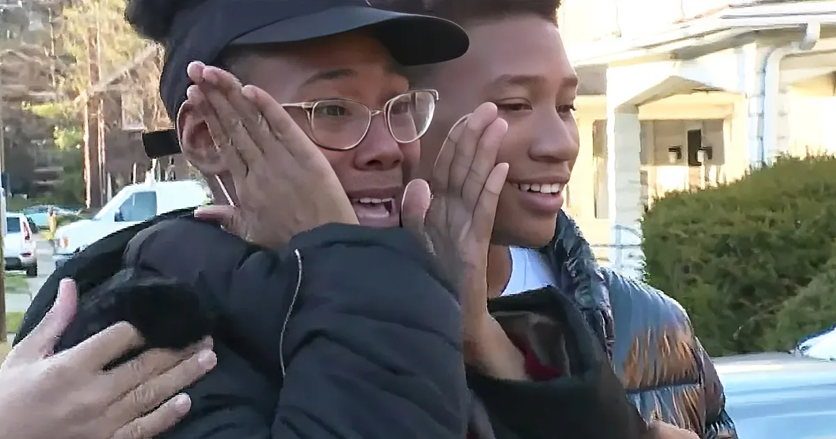 A woman in a black jacket and cap is embracing a young boy, both smiling and appearing happy.