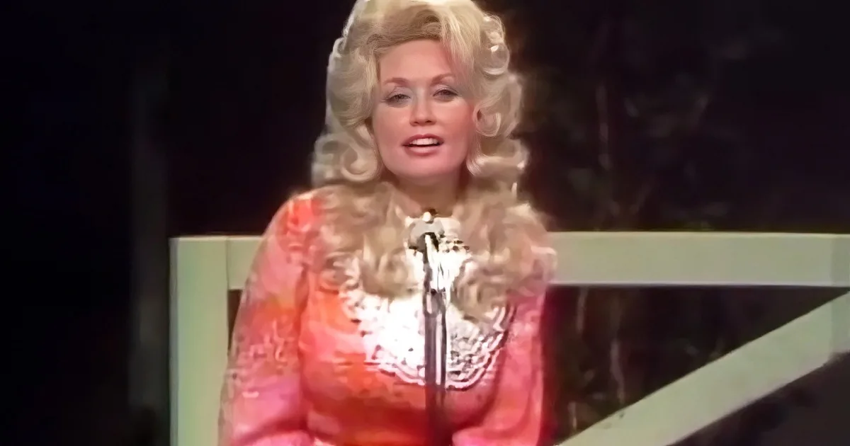 Dolly Parton in a vibrant orange outfit with a microphone, performing on stage.