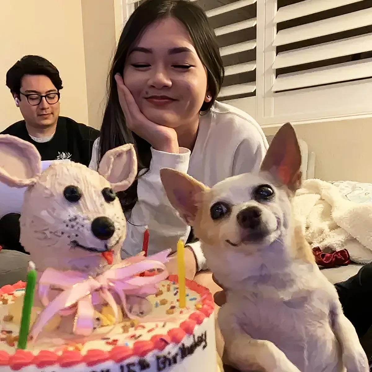 A small white dog with a birthday cake featuring its face, surrounded by people and a cozy setting.