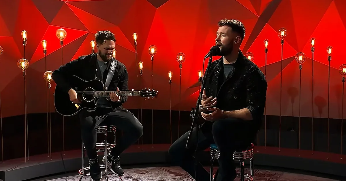 Two men perform on stage, one playing guitar, the other singing into a microphone.