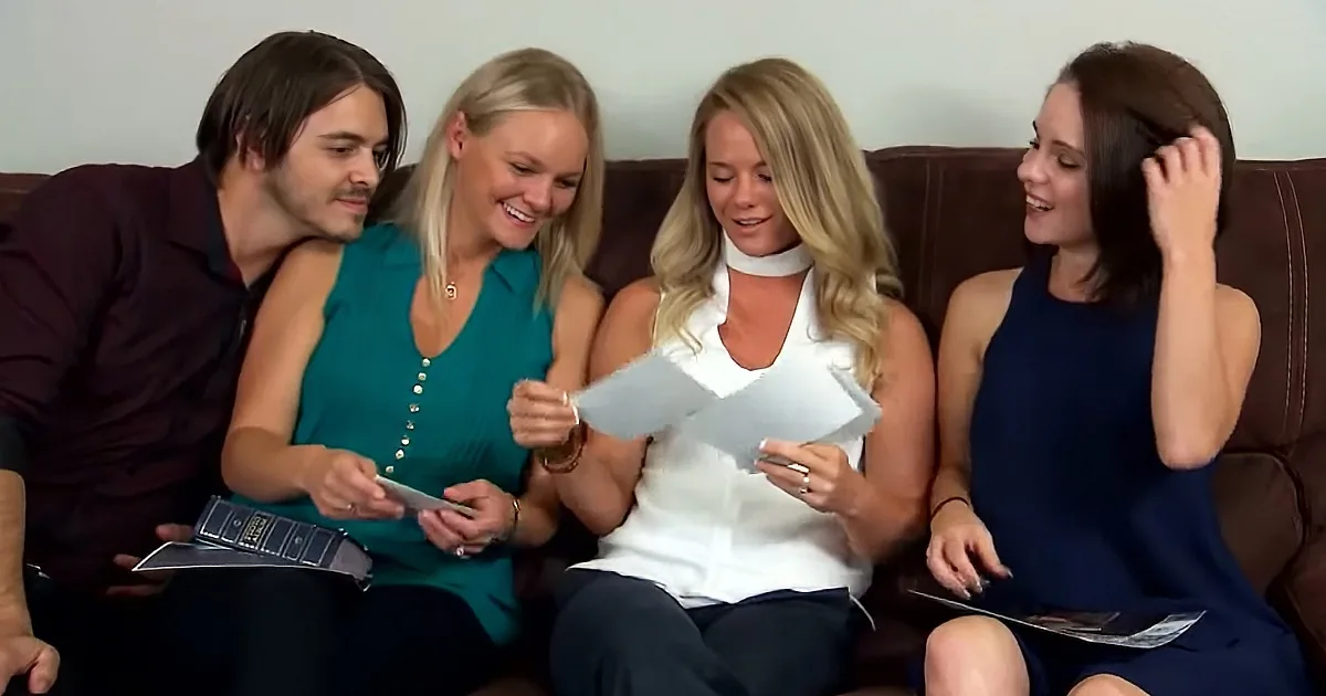 Four people sitting on a couch, three women and one man, holding papers and smiling.